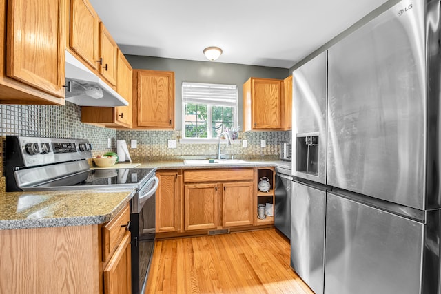 kitchen featuring light wood-style flooring, under cabinet range hood, a sink, stainless steel appliances, and decorative backsplash