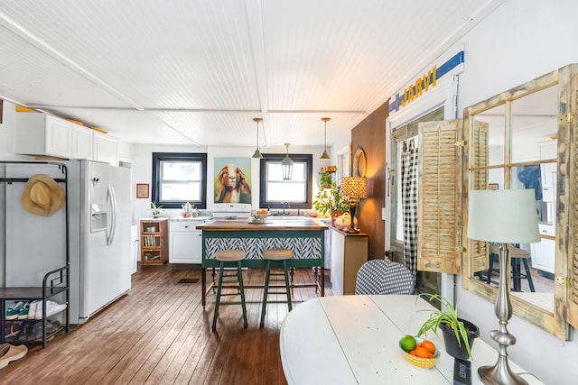 kitchen with white cabinets, white fridge with ice dispenser, dark wood-type flooring, a sink, and decorative light fixtures