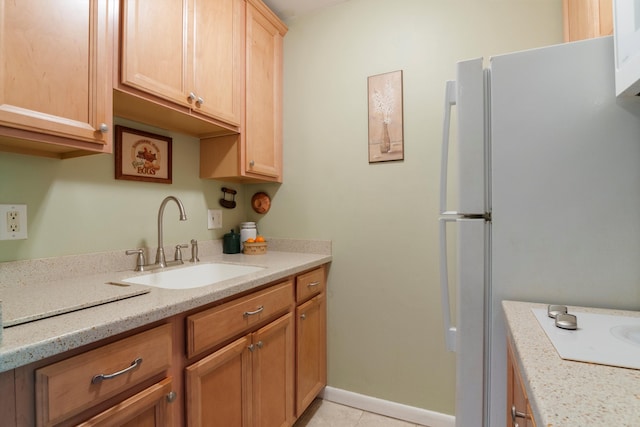 kitchen with baseboards, a sink, light tile patterned flooring, light stone counters, and freestanding refrigerator