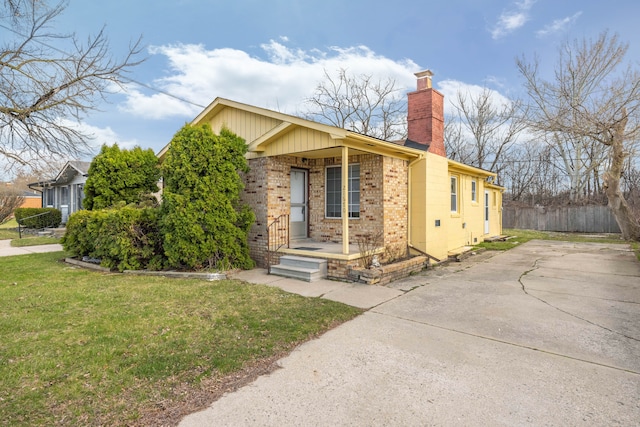 view of front of property with concrete driveway, a chimney, a front yard, brick siding, and fence