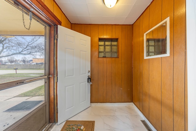 doorway to outside with marble finish floor and wooden walls