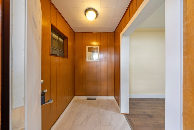 doorway featuring wooden walls, baseboards, and marble finish floor