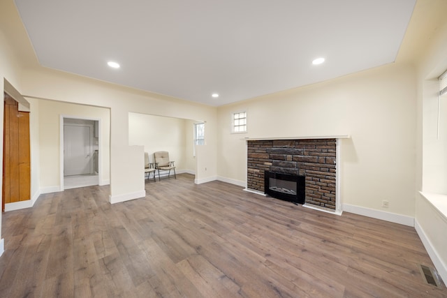 unfurnished living room with a fireplace, visible vents, baseboards, and wood finished floors