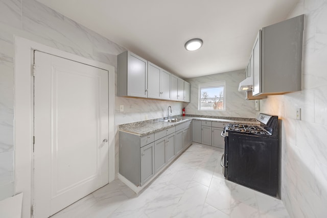 kitchen featuring under cabinet range hood, gray cabinets, decorative backsplash, marble finish floor, and gas range oven