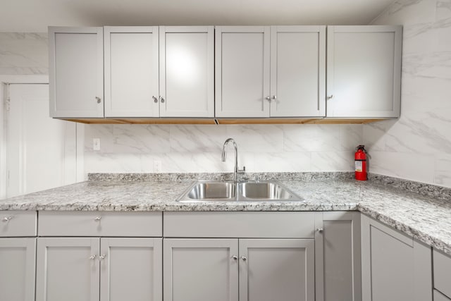 kitchen with light stone counters, a sink, and backsplash