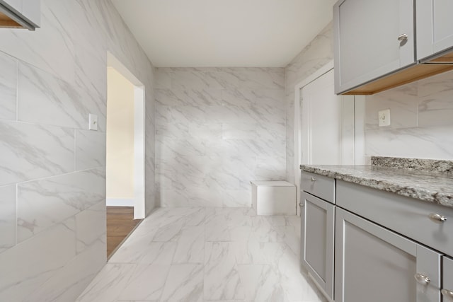 bathroom featuring marble finish floor, toilet, vanity, and tile walls