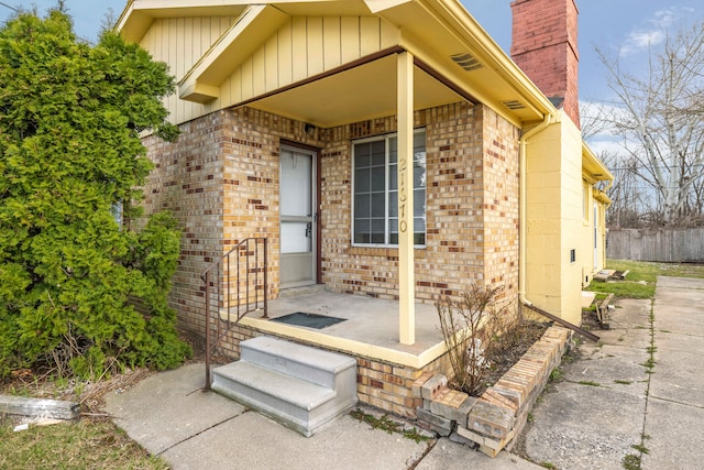 view of exterior entry with brick siding, board and batten siding, and a chimney