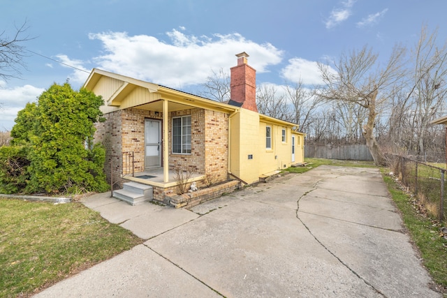 view of side of home with concrete driveway, brick siding, fence, and a chimney