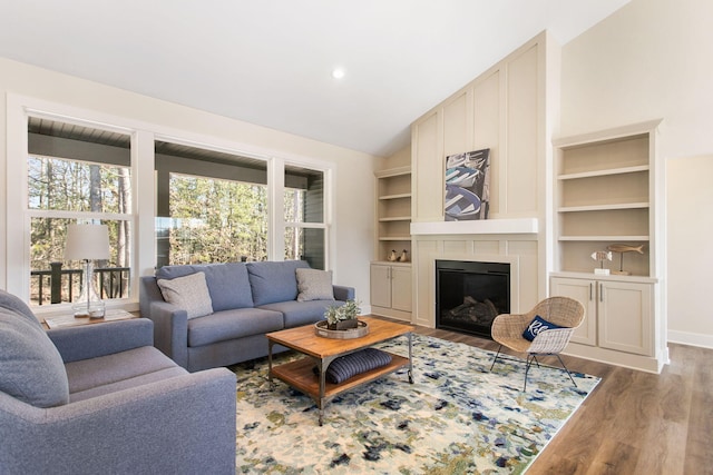 living area with lofted ceiling, wood finished floors, a glass covered fireplace, and built in shelves