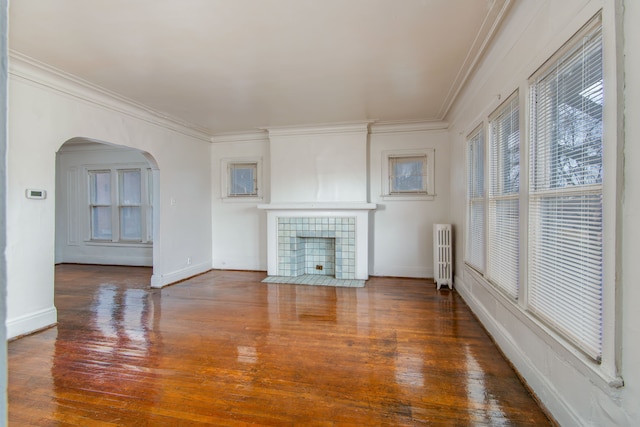 unfurnished living room with arched walkways, wood finished floors, radiator heating unit, and crown molding