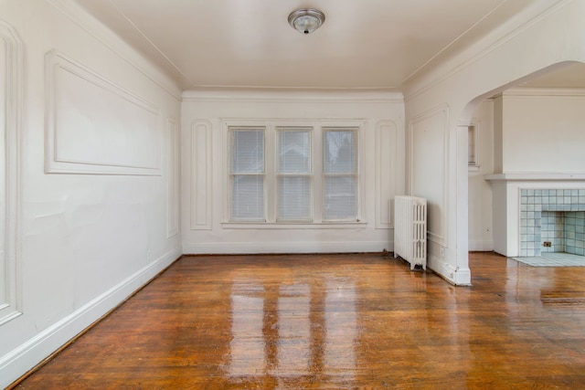 spare room featuring crown molding, wood finished floors, radiator, baseboards, and arched walkways