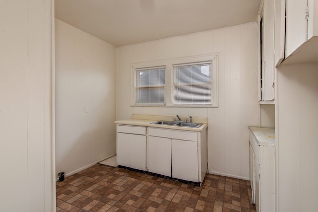 kitchen featuring brick floor, white cabinets, light countertops, and a sink