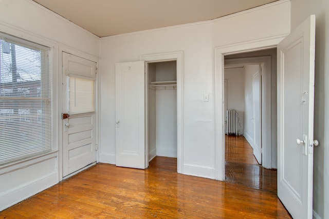 unfurnished bedroom with a closet, baseboards, wood finished floors, and radiator heating unit