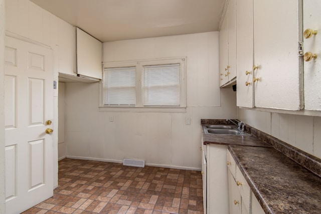 kitchen featuring white cabinets, a sink, dark countertops, and visible vents