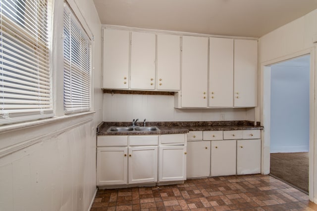 kitchen with brick floor, white cabinets, dark countertops, and a sink
