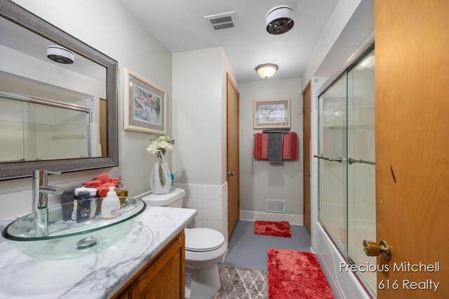 full bath with toilet, vanity, shower / bath combination with glass door, and visible vents