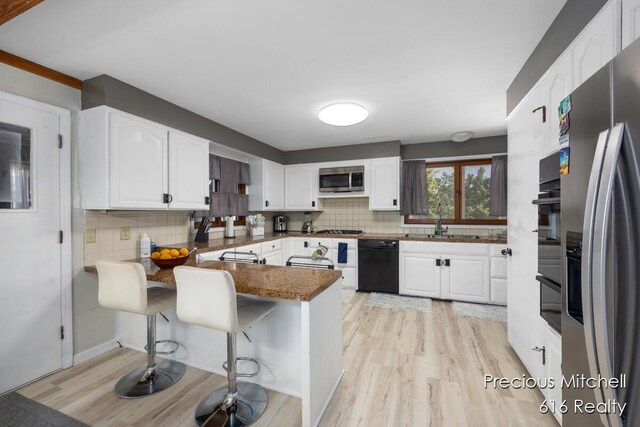 kitchen featuring white cabinets, a peninsula, stainless steel appliances, and tasteful backsplash