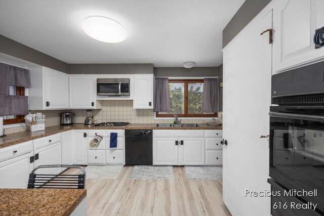 kitchen featuring a sink, white cabinets, tasteful backsplash, light wood-style flooring, and black appliances