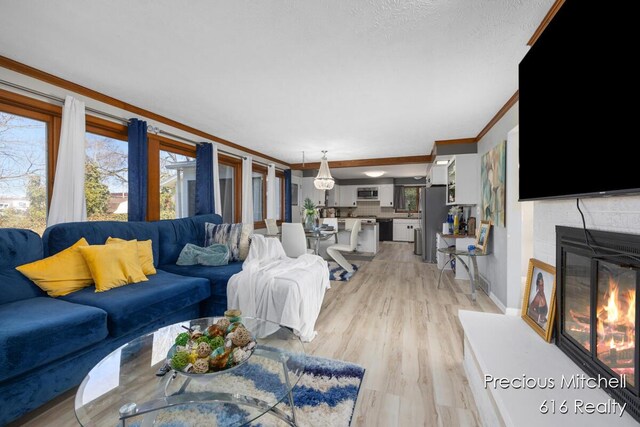 living room with ornamental molding, a glass covered fireplace, and light wood-style floors