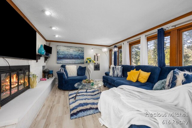 living area featuring wood finished floors, a textured ceiling, a brick fireplace, baseboards, and ornamental molding