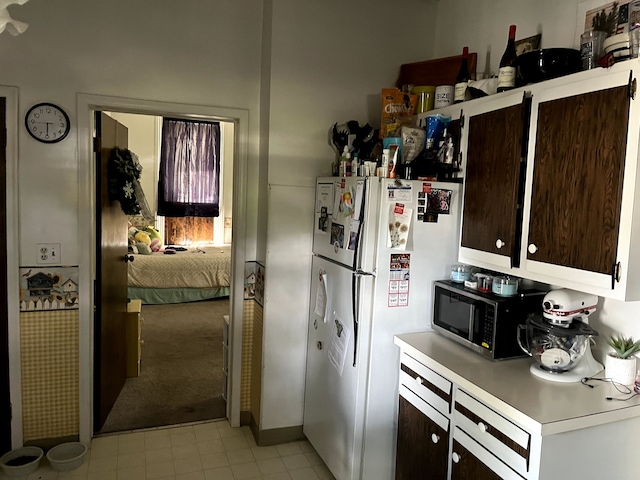 kitchen with stainless steel microwave, light countertops, dark brown cabinetry, and freestanding refrigerator