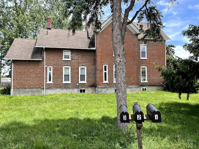 rear view of property with brick siding, a lawn, roof with shingles, and a chimney