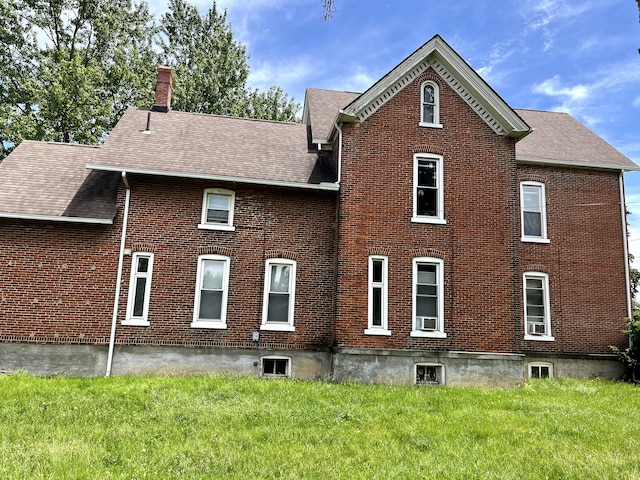 rear view of property featuring brick siding, a shingled roof, a yard, and a chimney