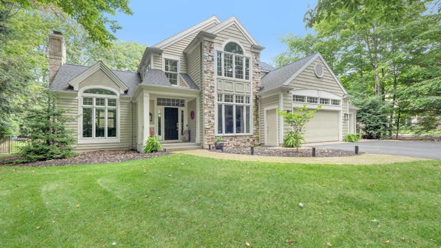 view of front of house with driveway, a chimney, a front lawn, a shingled roof, and stone siding