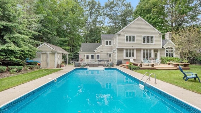 rear view of house with a wooden deck, outdoor lounge area, an outdoor pool, a lawn, and an outdoor structure