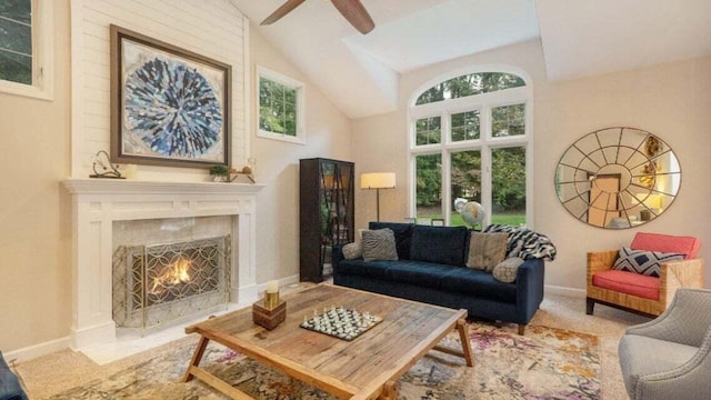 living area with a ceiling fan, baseboards, a fireplace with flush hearth, and high vaulted ceiling