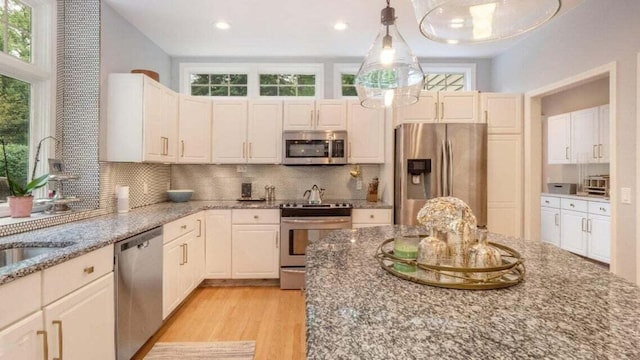 kitchen with appliances with stainless steel finishes, backsplash, light wood-type flooring, and a wealth of natural light