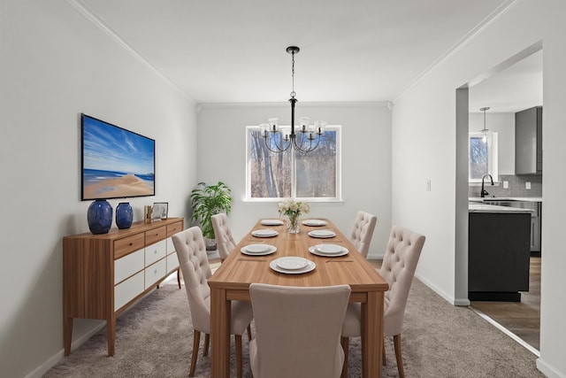 carpeted dining area with baseboards, a notable chandelier, crown molding, and a sink