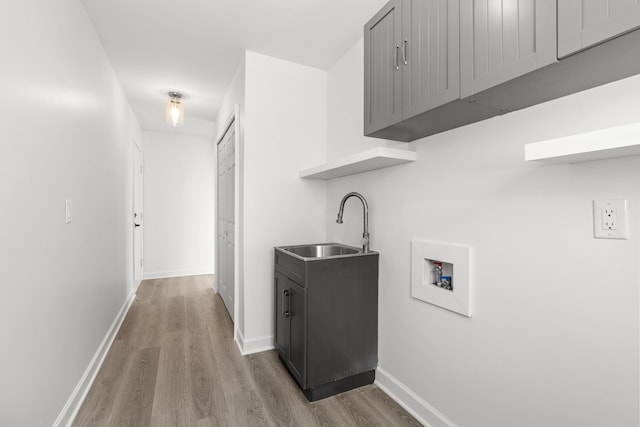 laundry room with baseboards, a sink, light wood-style floors, cabinet space, and washer hookup