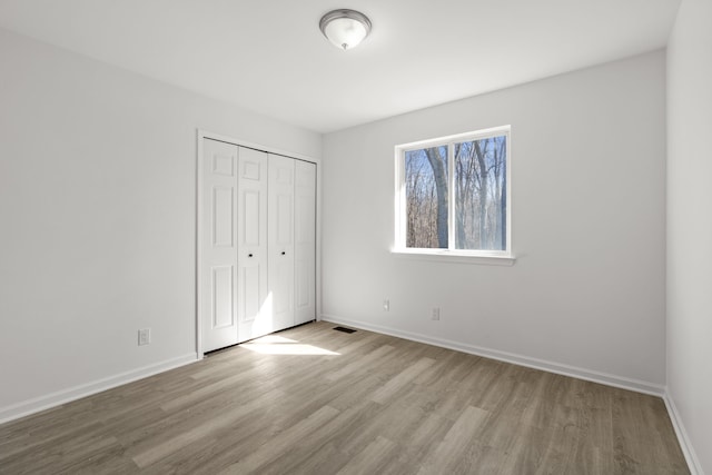 unfurnished bedroom with visible vents, baseboards, a closet, and wood finished floors