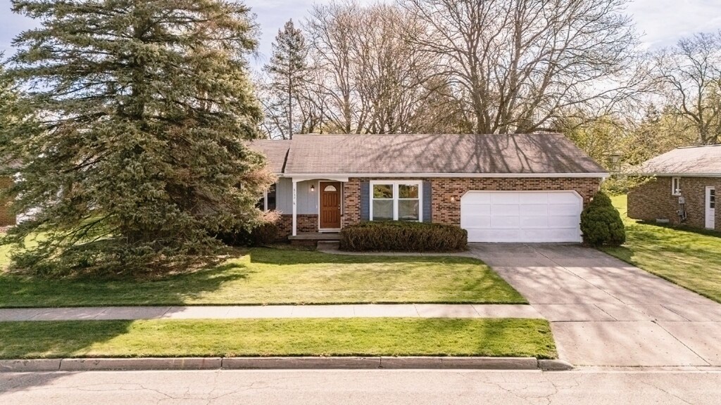 single story home with concrete driveway, a front yard, brick siding, and a garage