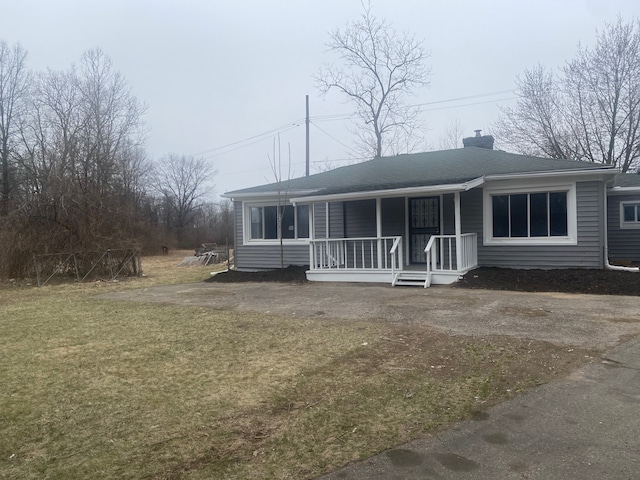 view of front facade with a shingled roof, a chimney, a porch, and a front yard