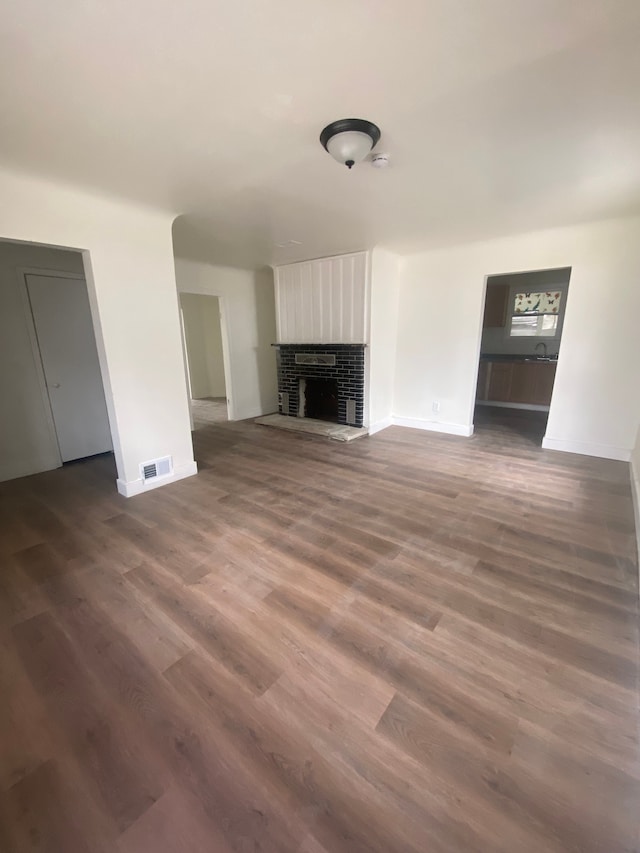 unfurnished living room featuring a brick fireplace, baseboards, visible vents, and dark wood-style floors