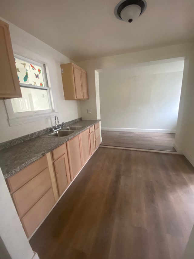 kitchen with dark wood-style flooring, dark countertops, a sink, baseboards, and light brown cabinets
