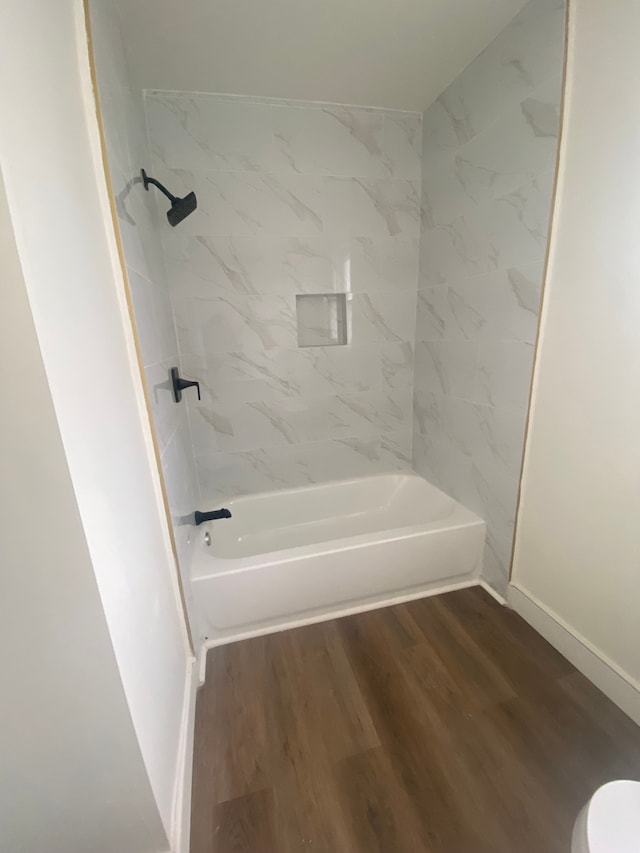 full bath featuring baseboards, washtub / shower combination, wood finished floors, and toilet