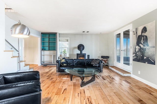 living area featuring french doors, light wood-style flooring, stairs, and a wood stove