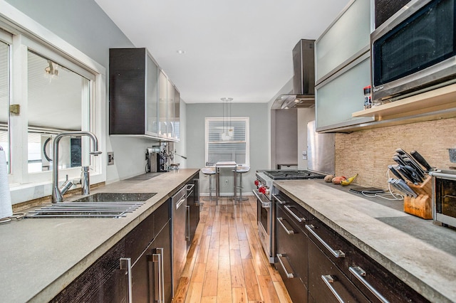 kitchen with light wood-type flooring, backsplash, a sink, appliances with stainless steel finishes, and wall chimney exhaust hood