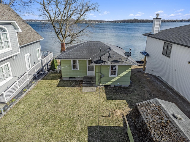 back of house featuring a chimney, roof with shingles, a water view, and a yard