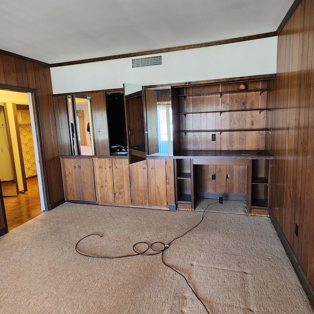 unfurnished living room featuring ornamental molding, wood walls, carpet flooring, and visible vents