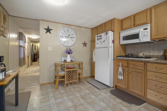 kitchen featuring wooden walls, brown cabinets, baseboards, white appliances, and decorative backsplash