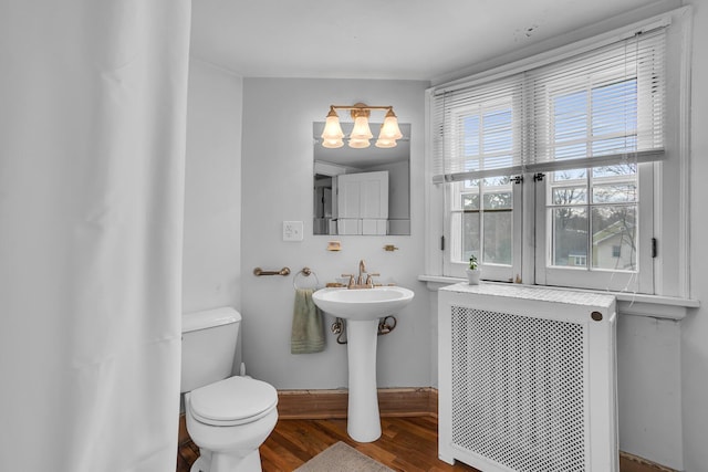 1515 W Franklin St, Jackson, MI 49203 - bathroom featuring baseboards, wood finished floors, radiator heating unit, toilet, and a notable chandelier
