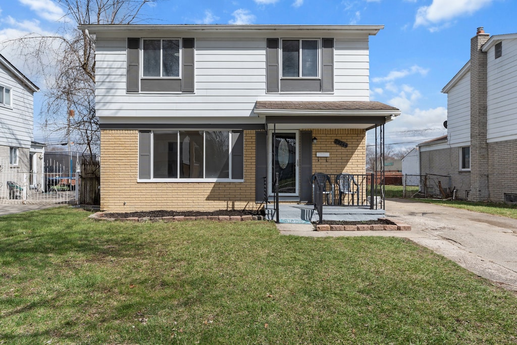 view of front of home featuring brick siding, a front lawn, fence, and concrete driveway