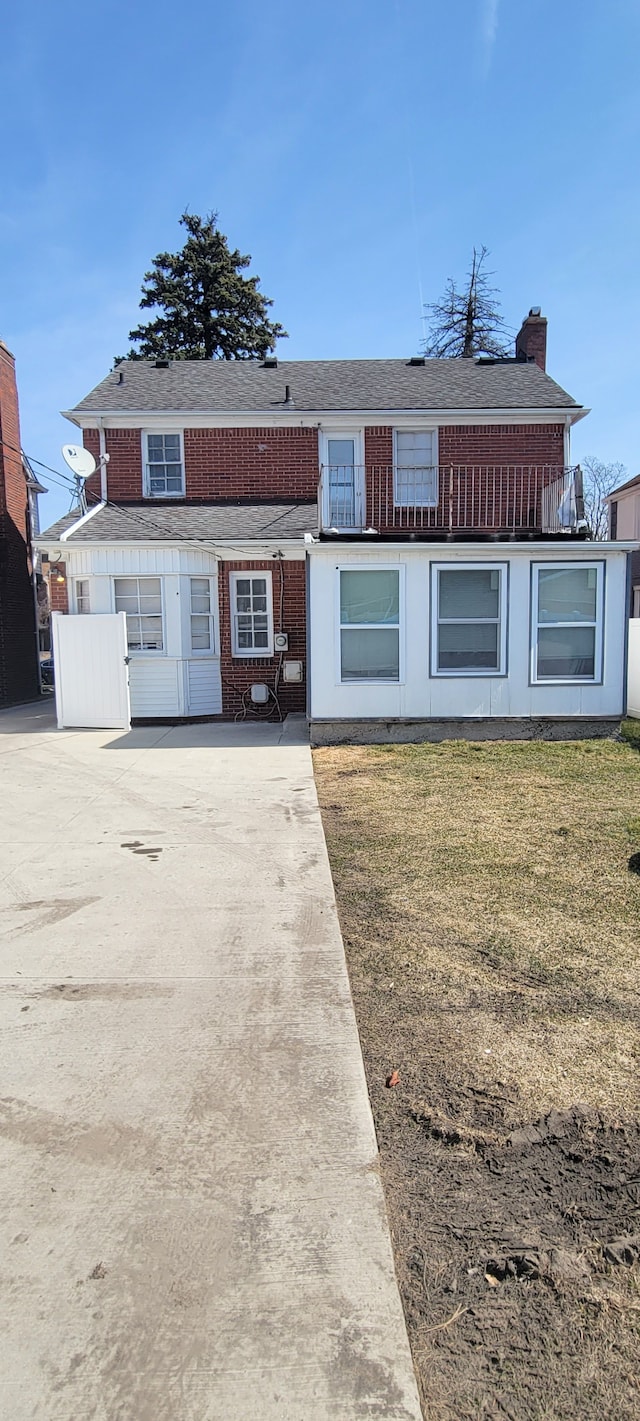view of property featuring concrete driveway, a chimney, a front lawn, a shingled roof, and brick siding