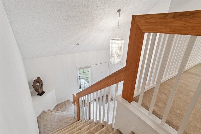 stairway with a chandelier, vaulted ceiling, and a textured ceiling