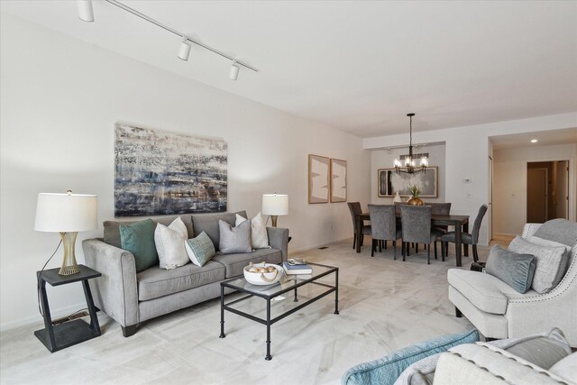 living room featuring baseboards, track lighting, a notable chandelier, and light colored carpet