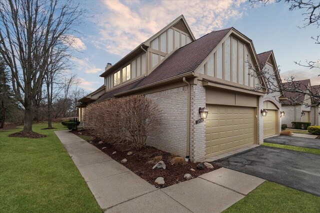 view of home's exterior featuring roof with shingles, a chimney, brick siding, aphalt driveway, and a lawn